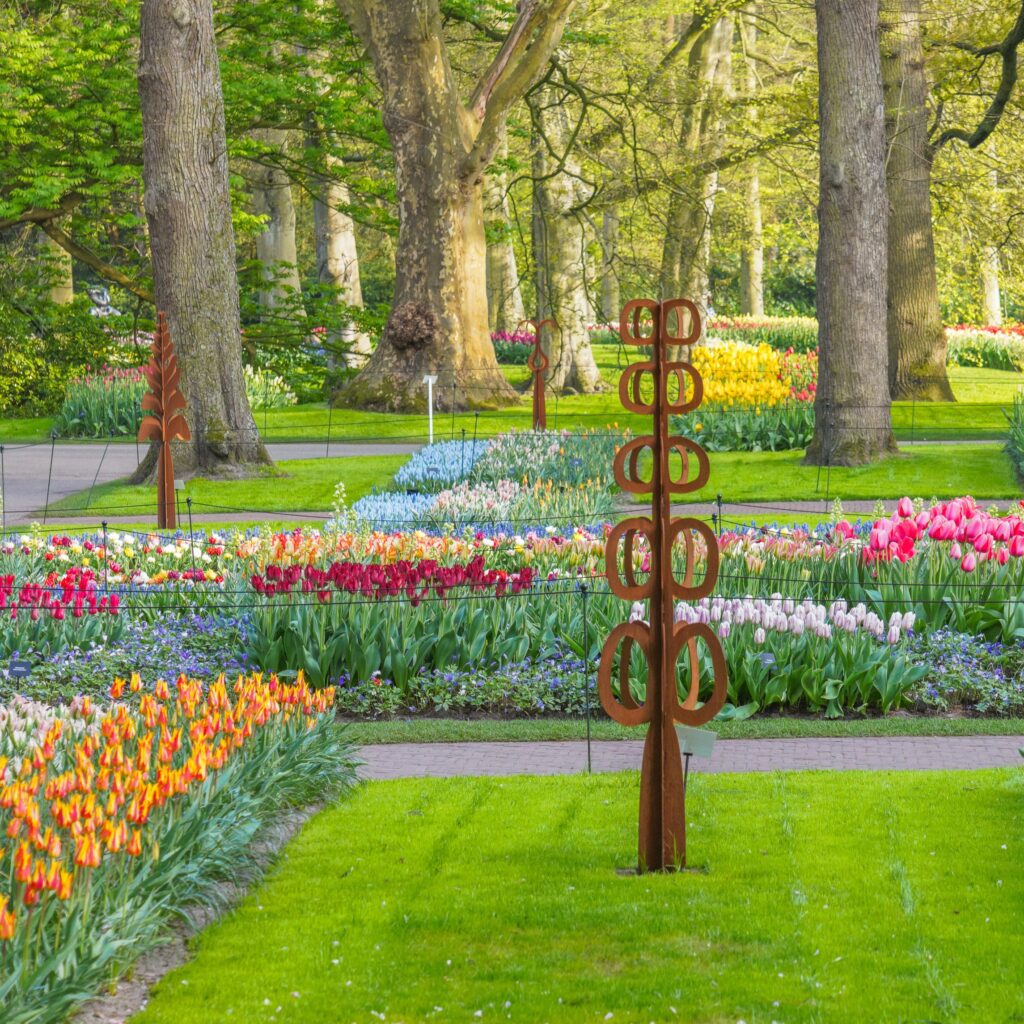 Sculptuur van cortenstaal in de vorm van een kiemende knop, roestbruin tegen het voorjaarsgroen.